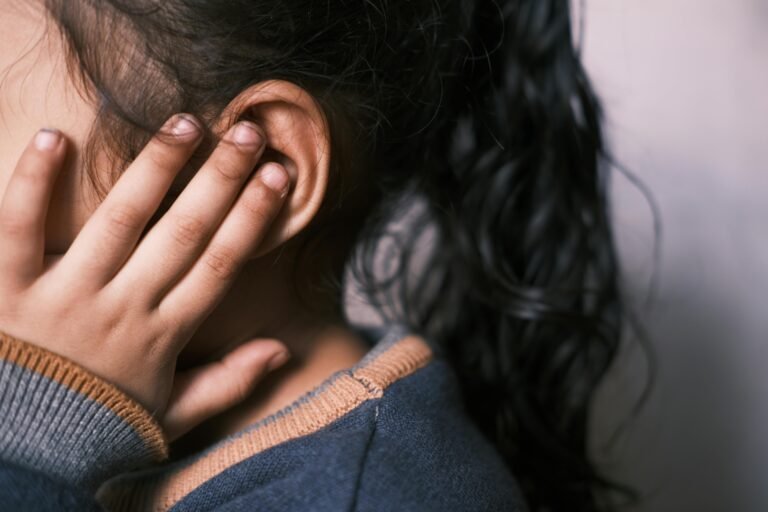 A young girl with long dark hair touching her ear to emphasize sound awareness.