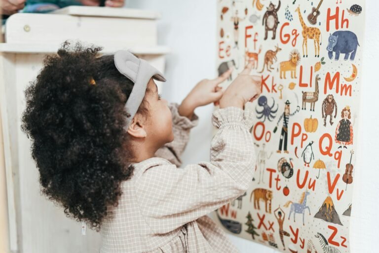 Child with curly hair points to an animal alphabet poster, learning letters and developing reading readiness.